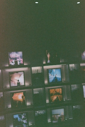 Several framed images and objects are arranged on illuminated shelves against a dark background. Some of the images include natural landscapes and artistic compositions, creating a curated and artistic display.