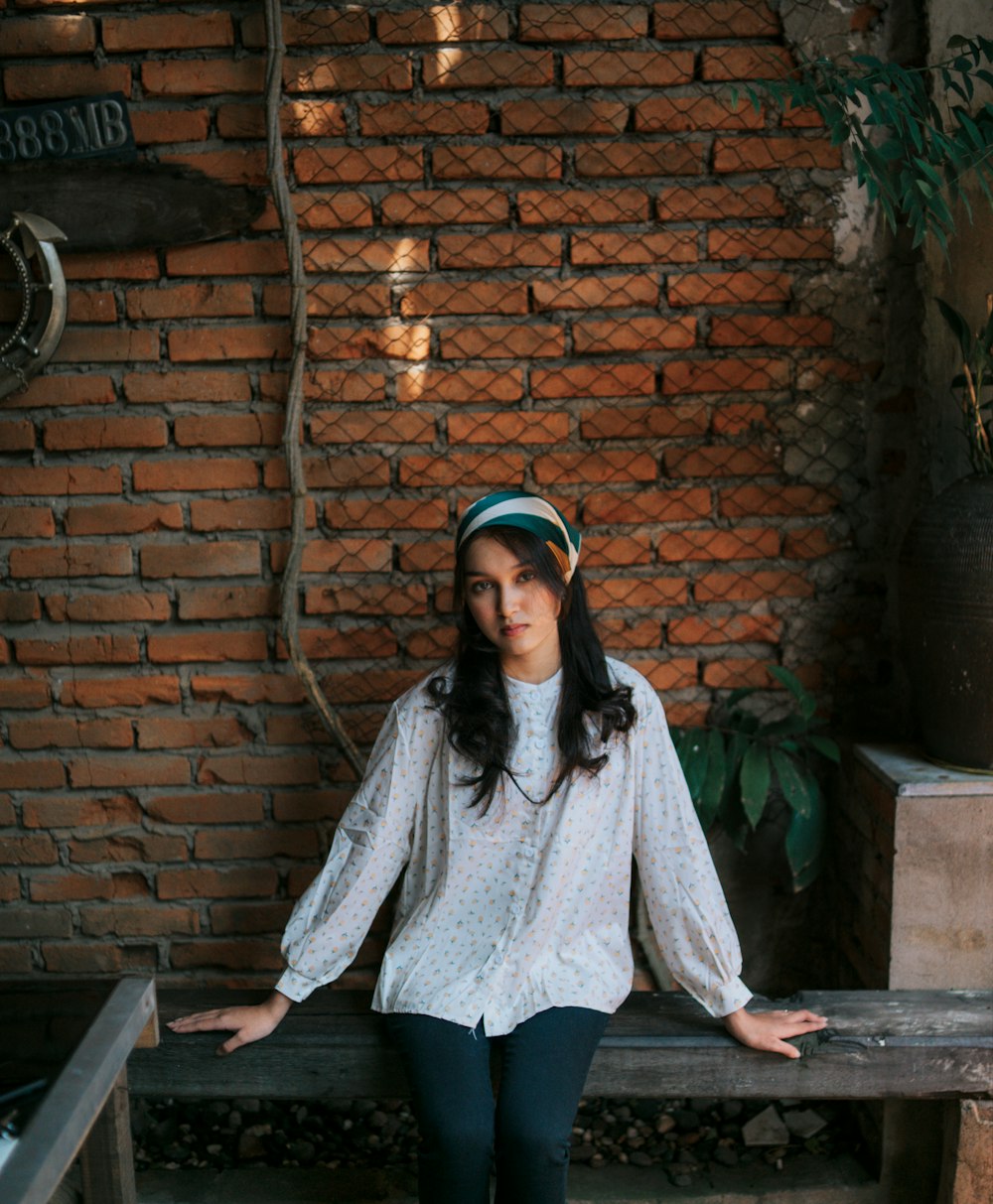 a woman sitting on a bench in front of a brick wall