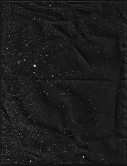 A textured black background is speckled with small white dots, resembling a star-filled night sky.