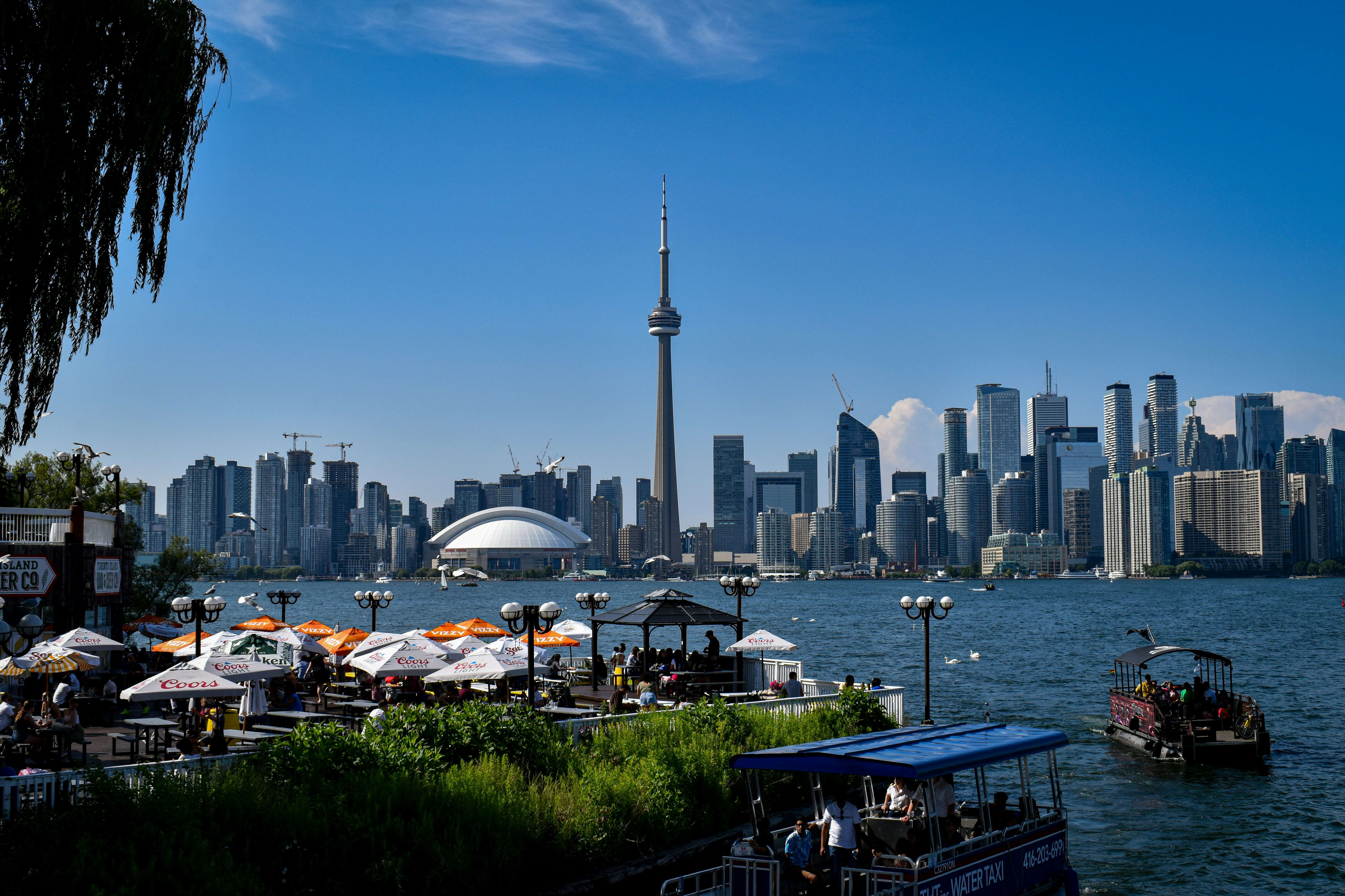 Toronto skyline viewed from a Toronto Islands pub-style restaurant, the CN Tower and downtown buildings visible against a blue sky
