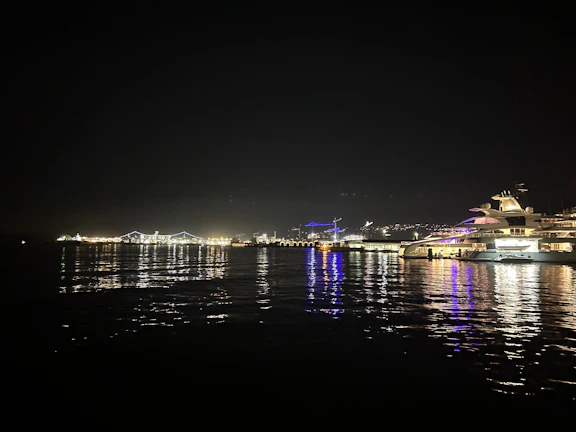 Nighttime shot of a ship navigating through calm waters with city lights in the background.