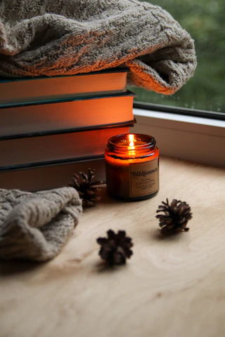 A cozy corner with a stack of inspirational books and a journal beside a glowing candle.