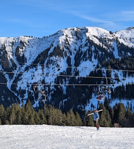A friendly ski sherpa carrying a child's skis and boots from a snowy parking lot.