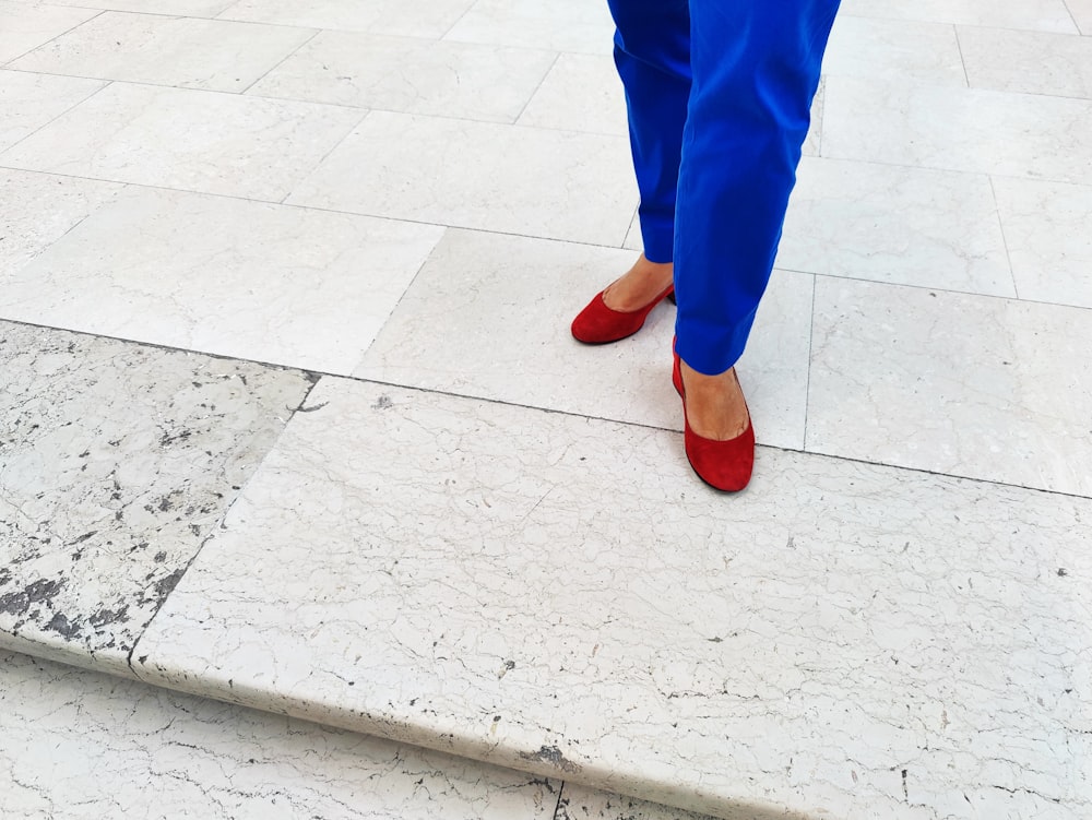 a woman in blue pants and red shoes standing on a stone step