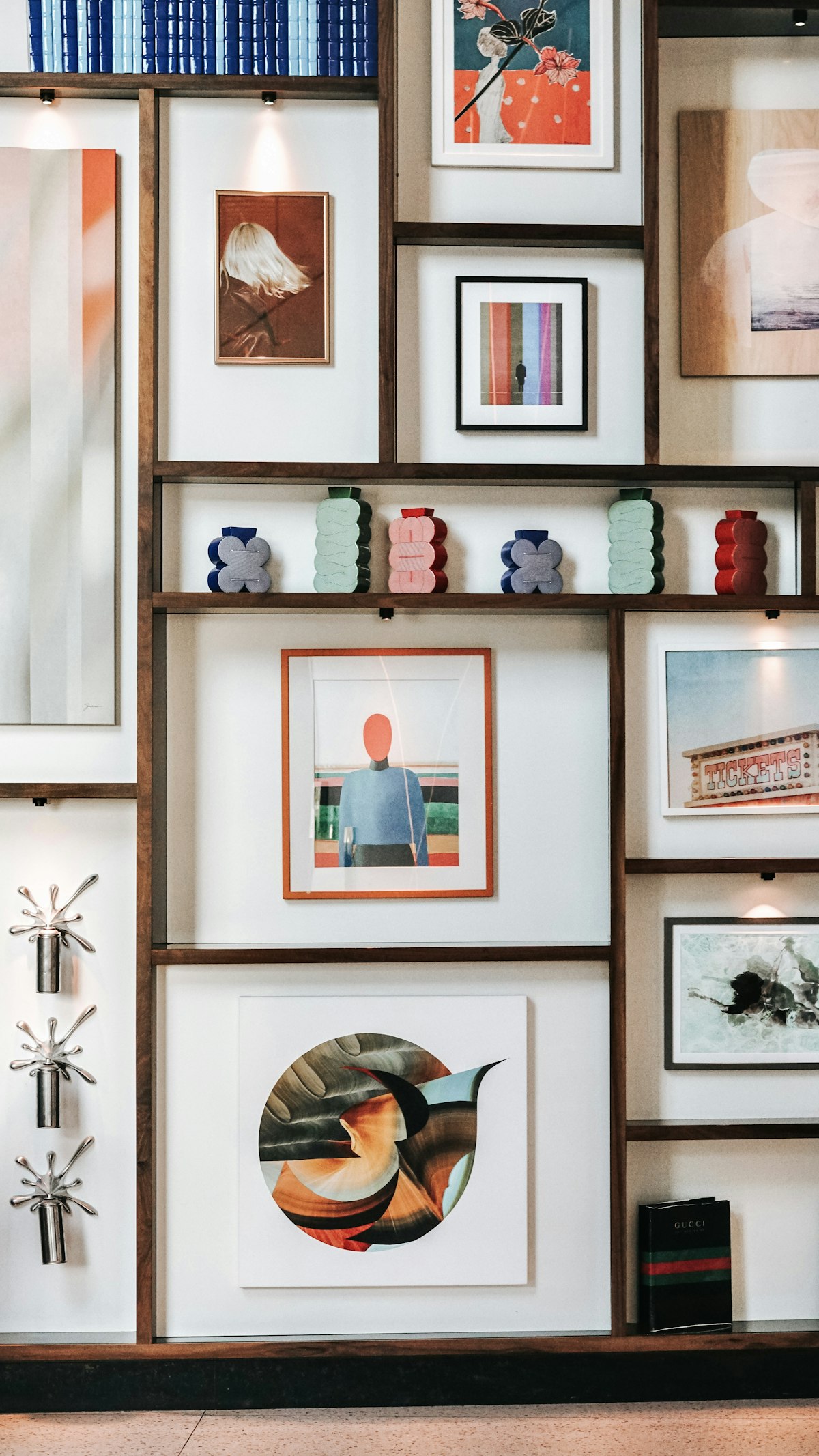 A wall of framed prints in different sizes, lit from above