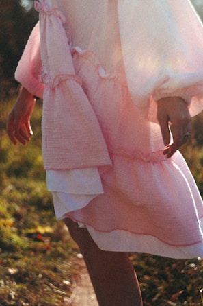 A model showcasing a flowing, elegant dress in a sunny park.