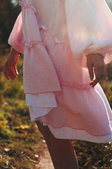 A model wearing a chic, flowing dress in soft pastel tones, standing in a sunlit urban park.