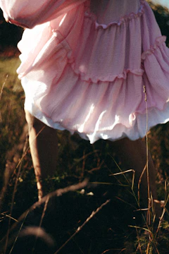 A model wearing a dusty blush flowy dress standing in a sunlit meadow.