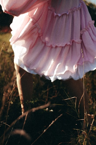 A model wearing a chic western dress in pastel pink, standing gracefully against a sunlit garden backdrop.