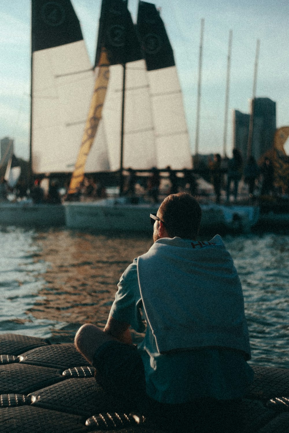 a man sitting on the edge of a boat looking at a sailboat