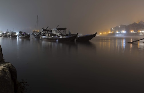 Nighttime shot of boats lit by lanterns floating on a peaceful river.