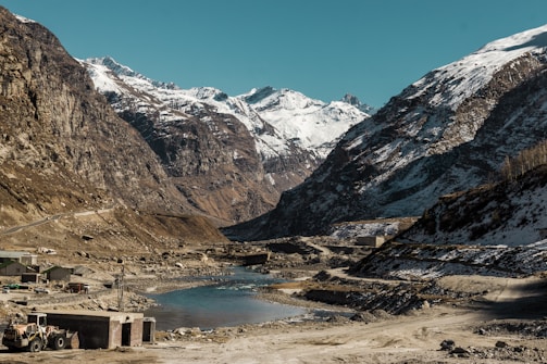 Engineers surveying a remote Himalayan road construction site surrounded by snowy peaks.