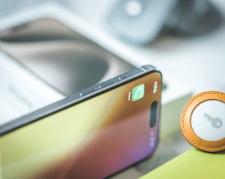 A smartphone with a call notification displayed on its screen. The device is placed on a surface alongside an item that resembles a keychain with a circular design. The background is blurred, showing parts of other objects.
