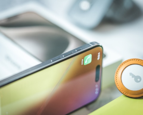 A smartphone with a call notification displayed on its screen. The device is placed on a surface alongside an item that resembles a keychain with a circular design. The background is blurred, showing parts of other objects.