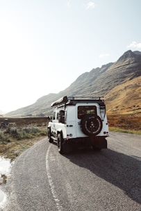 A rugged 4x4 vehicle parked beside a mountain trail under a clear blue sky.