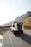 A rugged SUV driving along a scenic mountain road under a clear blue sky.