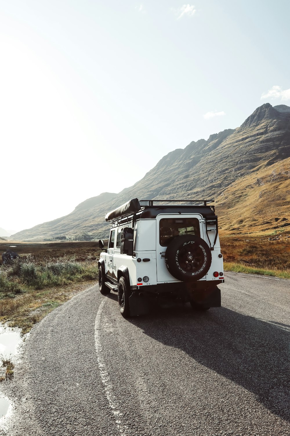 a white vehicle driving down a road next to a mountain