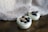 Two small glass bowls filled with white yogurt are topped with fresh blueberries and a sprinkle of brown powder, possibly cinnamon. The bowls rest on a wooden surface with a soft, fuzzy gray fabric in the background, giving a cozy and inviting appearance.