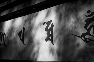 Black and white image featuring painted calligraphy on a wall, with shadows creating an abstract pattern across the surface.