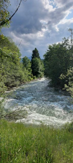 Researchers setting up equipment beside a flowing river under a cloudy sky.