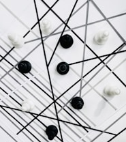 Chess pieces are arranged on a geometric background with intersecting black and gray lines. The pieces are predominantly black and white, creating a contrast against the patterned backdrop.