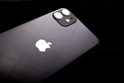 A black smartphone featuring a dual-lens camera and the iconic white apple logo. The device is slightly tilted against a dark background, highlighting its sleek and glossy finish.