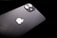 A black smartphone featuring a dual-lens camera and the iconic white apple logo. The device is slightly tilted against a dark background, highlighting its sleek and glossy finish.