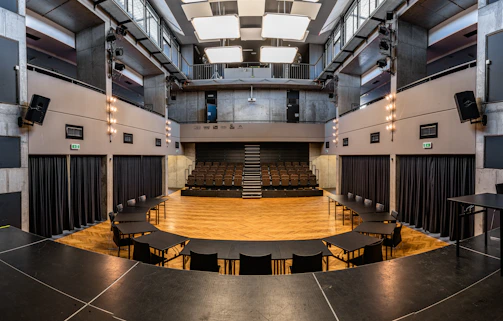 A wide shot of a minimalist theater stage with soft white curtains and subtle charcoal accents.