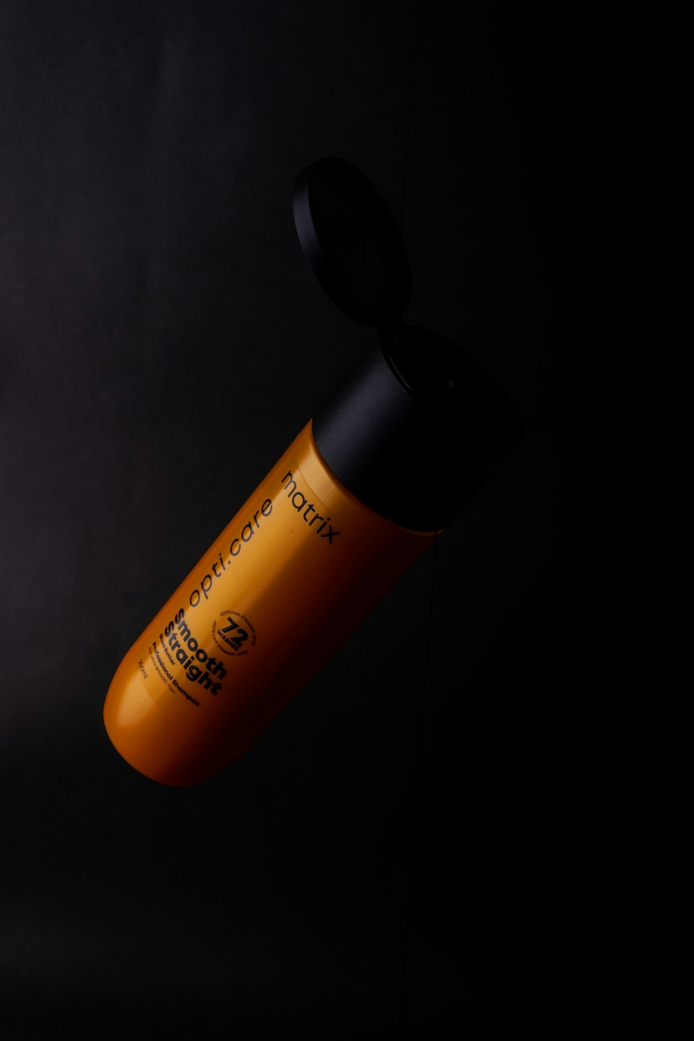 an orange bottle with a black cap on a black background