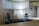 A modern office space with minimalistic design, featuring two office chairs, a sleek table, a storage cabinet, and a floor lamp. The room is decorated with light-colored curtains and has a polished concrete ceiling. The overall ambiance is professional and clean.