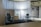 A modern office space with minimalistic design, featuring two office chairs, a sleek table, a storage cabinet, and a floor lamp. The room is decorated with light-colored curtains and has a polished concrete ceiling. The overall ambiance is professional and clean.