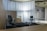 A modern office space with minimalistic design, featuring two office chairs, a sleek table, a storage cabinet, and a floor lamp. The room is decorated with light-colored curtains and has a polished concrete ceiling. The overall ambiance is professional and clean.