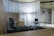 A modern office space with minimalistic design, featuring two office chairs, a sleek table, a storage cabinet, and a floor lamp. The room is decorated with light-colored curtains and has a polished concrete ceiling. The overall ambiance is professional and clean.