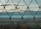 A wire mesh fence is in clear focus with a blurred landscape of rolling hills and a cloudy sky in the background.