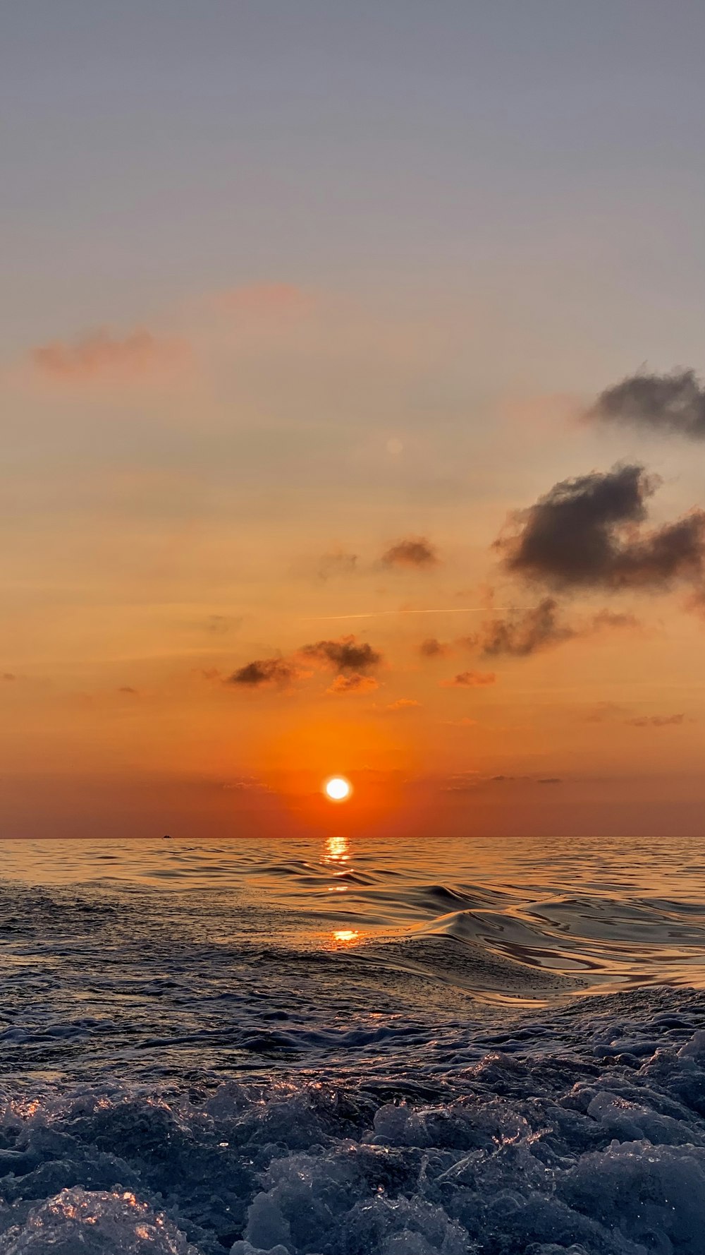 the sun is setting over the ocean on a cloudy day