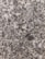 A close-up view of polished granite with a speckled pattern. The surface displays a mix of gray, white, black, and hints of pinkish tones, typical of natural stone with irregularly shaped dots and spots.