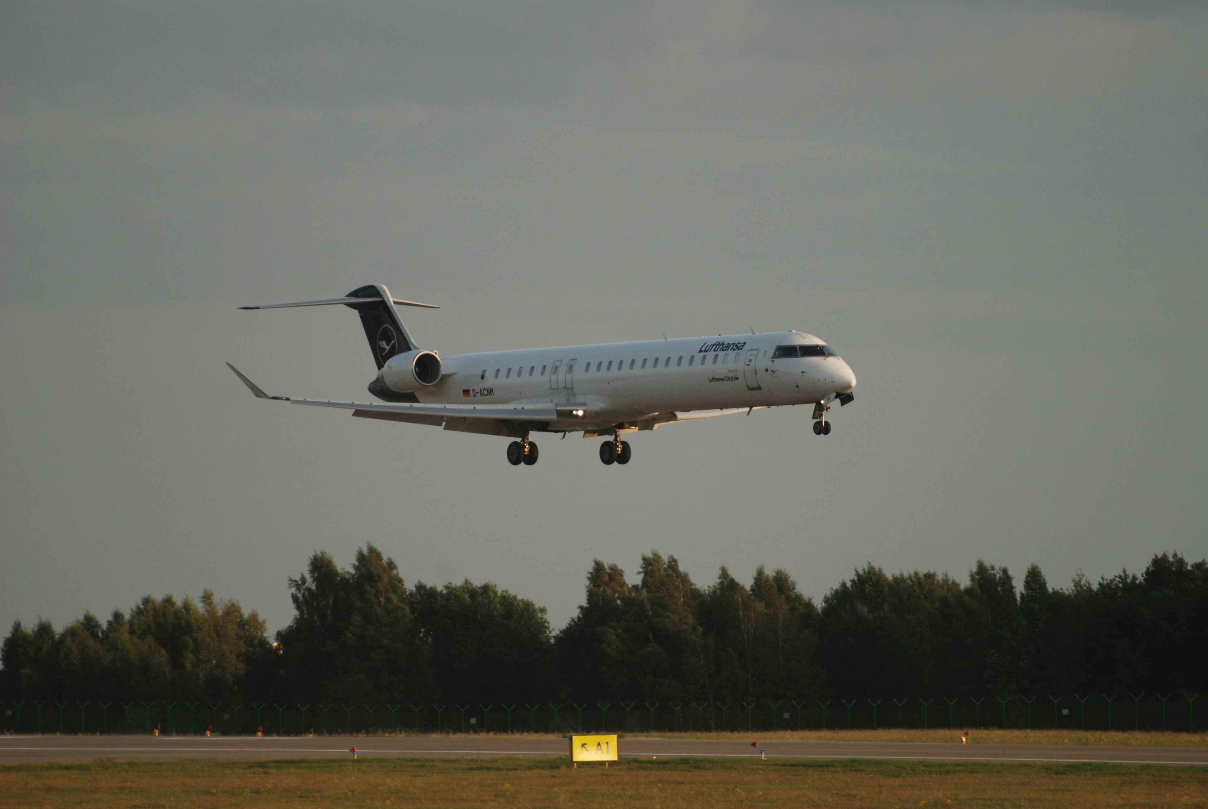 a large jetliner flying through a cloudy sky, Lufthansa Mitsubishi CRJ900 landing in Gdańsk airport, taken with Nikon D80 and a 70-300mm Nikon zoom lens
