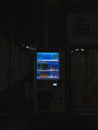 A sleek vending machine glowing softly with bioluminescent blue light in a dimly lit office lobby.