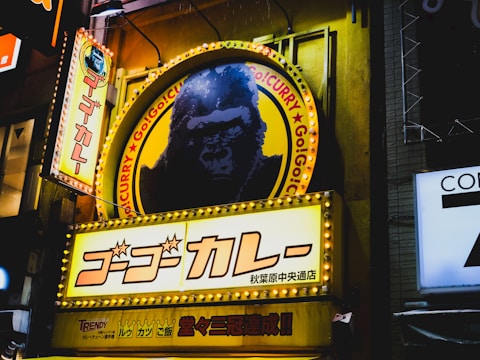 Brightly lit signs with Japanese writing and a dominant image of a gorilla on a circular sign. Surrounding neon lights enhance the visual appeal of a vibrant urban nightscape.