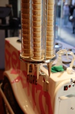 Stacks of ice cream cones are neatly arranged in a transparent vertical holder attached to an ice cream cart with tastefully designed graphics and branding.