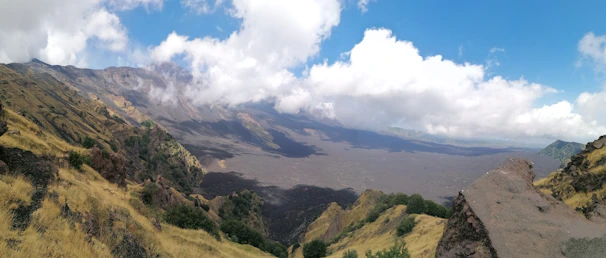 A panoramic view of volcanic mountains under a dramatic cloudy sky at dawn.