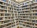 A library with rows of bookshelves filled with a variety of books organized by genre and author. A movable ladder provides access to books on higher shelves. The well-lit space has a clean and organized appearance.