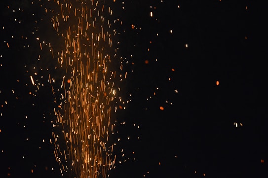 Bright, glowing orange sparks are scattered across a dark background, suggesting fireworks or sparklers in motion.