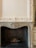 An ornate and intricately designed fireplace in a classic interior setting, featuring detailed carvings on the mantel and surrounding panel. The interior is dark with an imitation log and embers setup, suggesting a non-functional or decorative use.