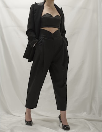 A sleek black jumpsuit styled with elegant heels and a clutch on a minimalist white background