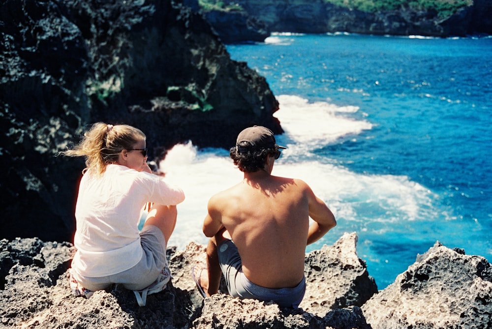 a man and a woman sitting on a cliff overlooking the ocean