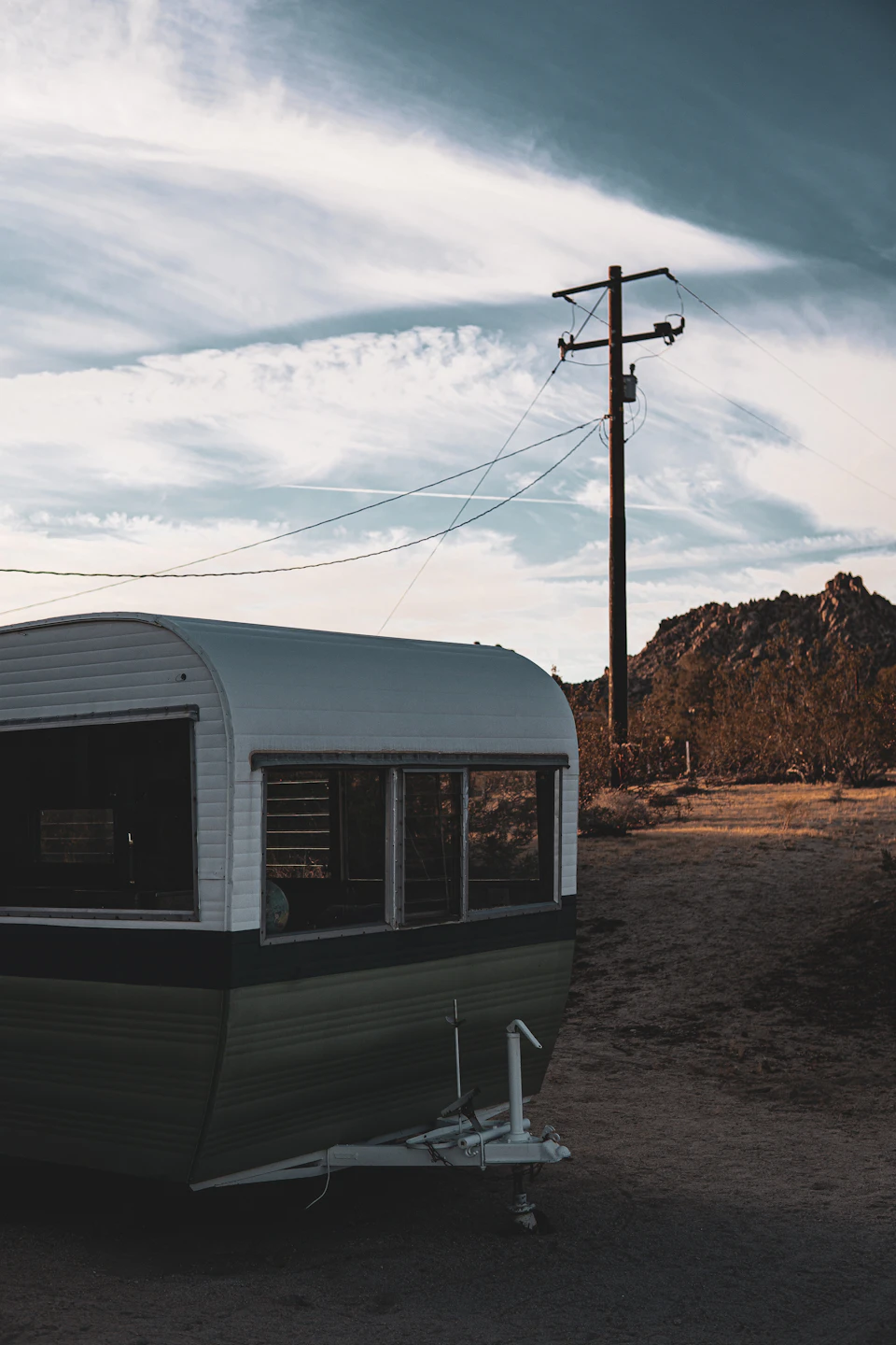 Vintage green and white trailer parked on dirt road facing right, towing behind vehicle