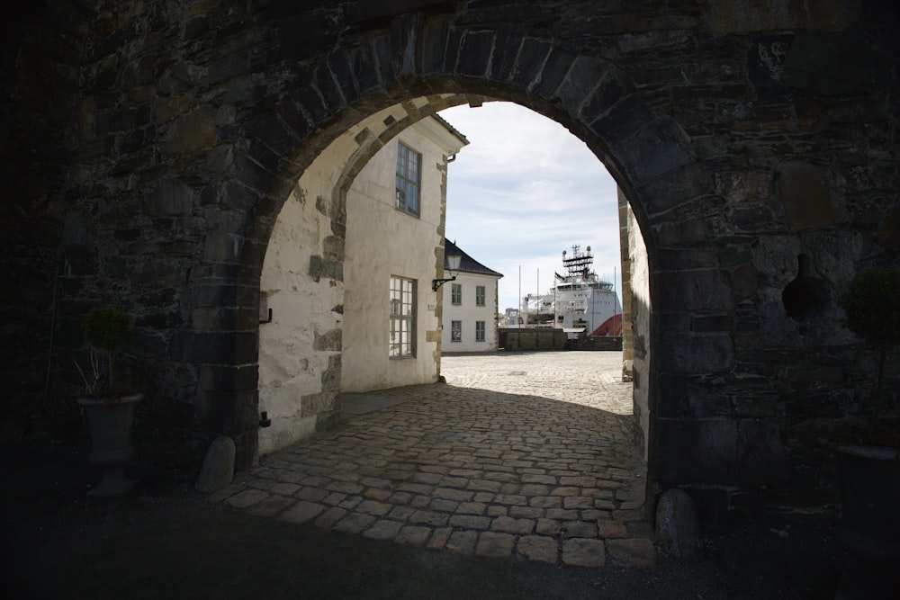 an archway leading to a building with a boat in the background