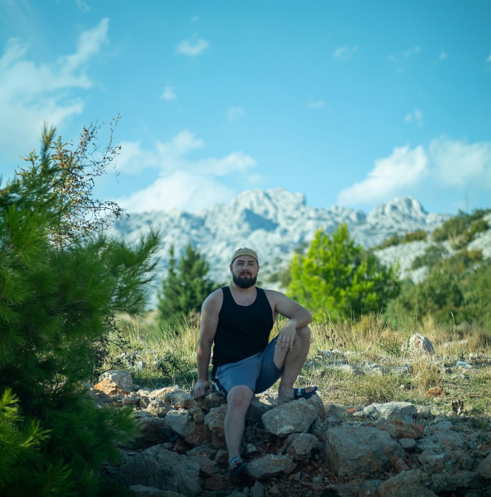 a man sitting on a pile of rocks with a mountain in the background