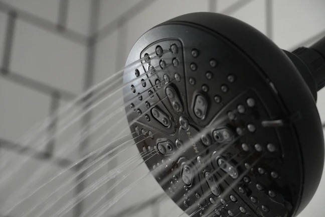 Close-up of the Purifit Premium black shower filter installed on a sleek modern showerhead with water gently flowing.